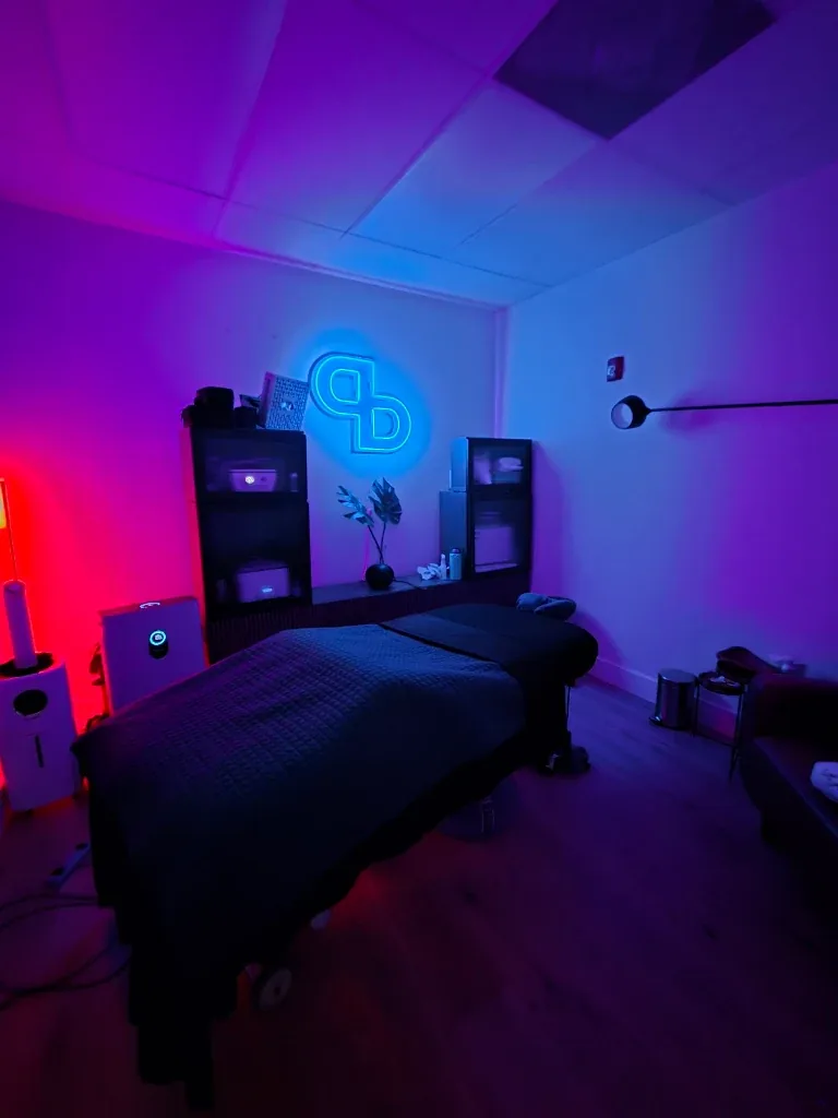 Pre Bodyworks treatment room lit in blue and magenta with the PB neon monogram on the wall